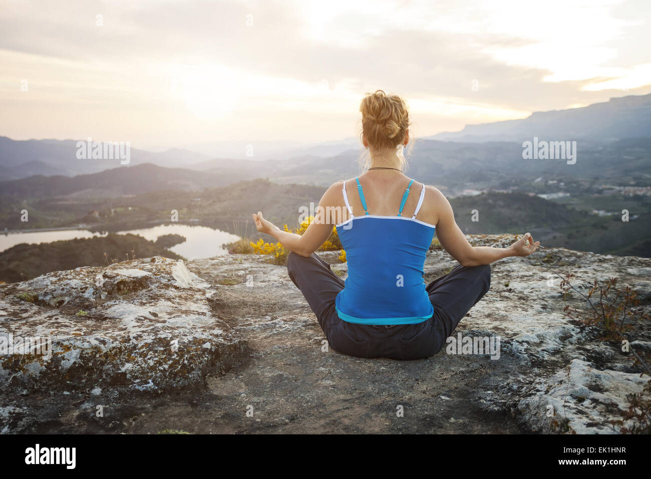 Young woman sitting on a rock and enjoying valley view. Girl sits in asana position. Stock Photo
