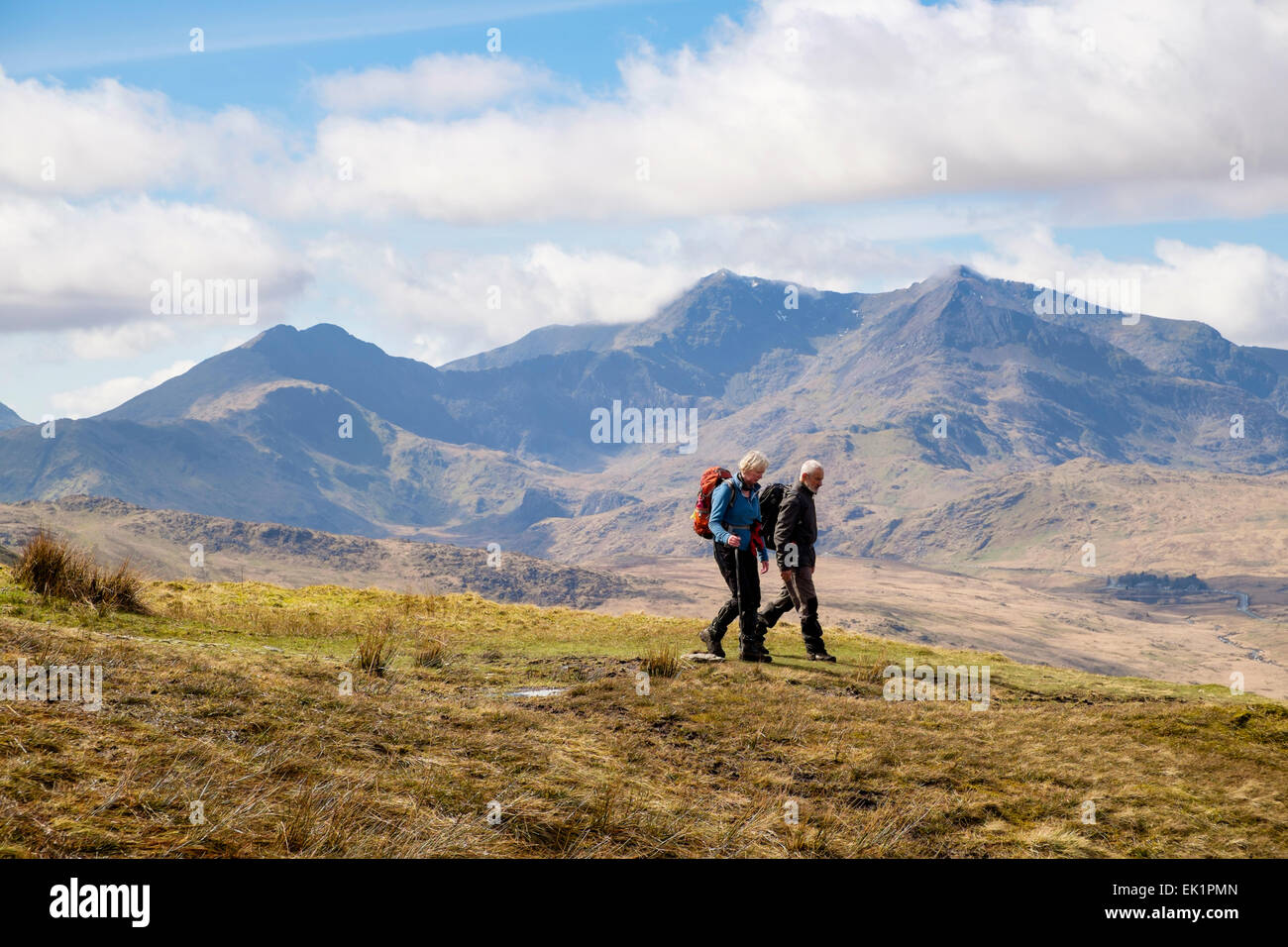 People hikers walking down on path from Moel Siabod to Capel Curig with view to the distant Mt Snowdon Horseshoe in Snowdonia (Eryri) Wales UK Britain Stock Photo