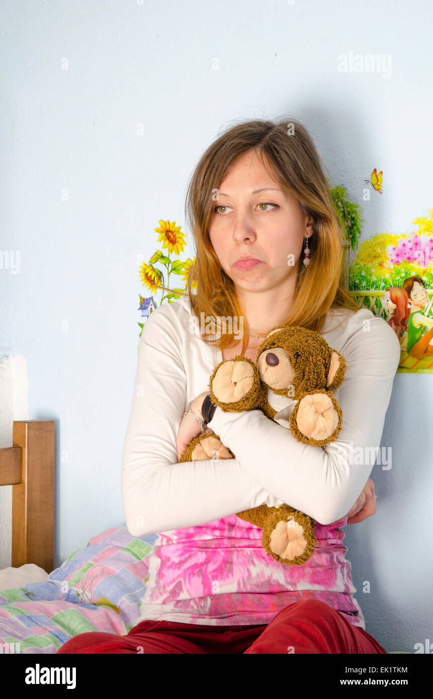 Sad girl hugging her toy bear on the bed Stock Photo
