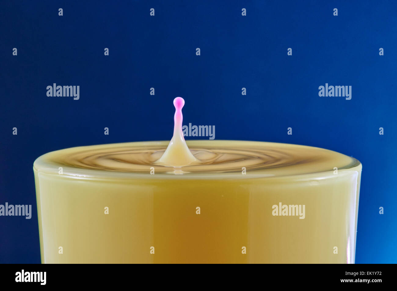 Pink drop splash in orange juice on blue background Stock Photo