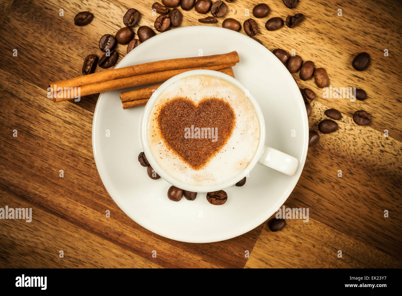 Cup of coffee with heart shape on foam served in porcelain saucer on wooden table. Shot from aerial view Stock Photo