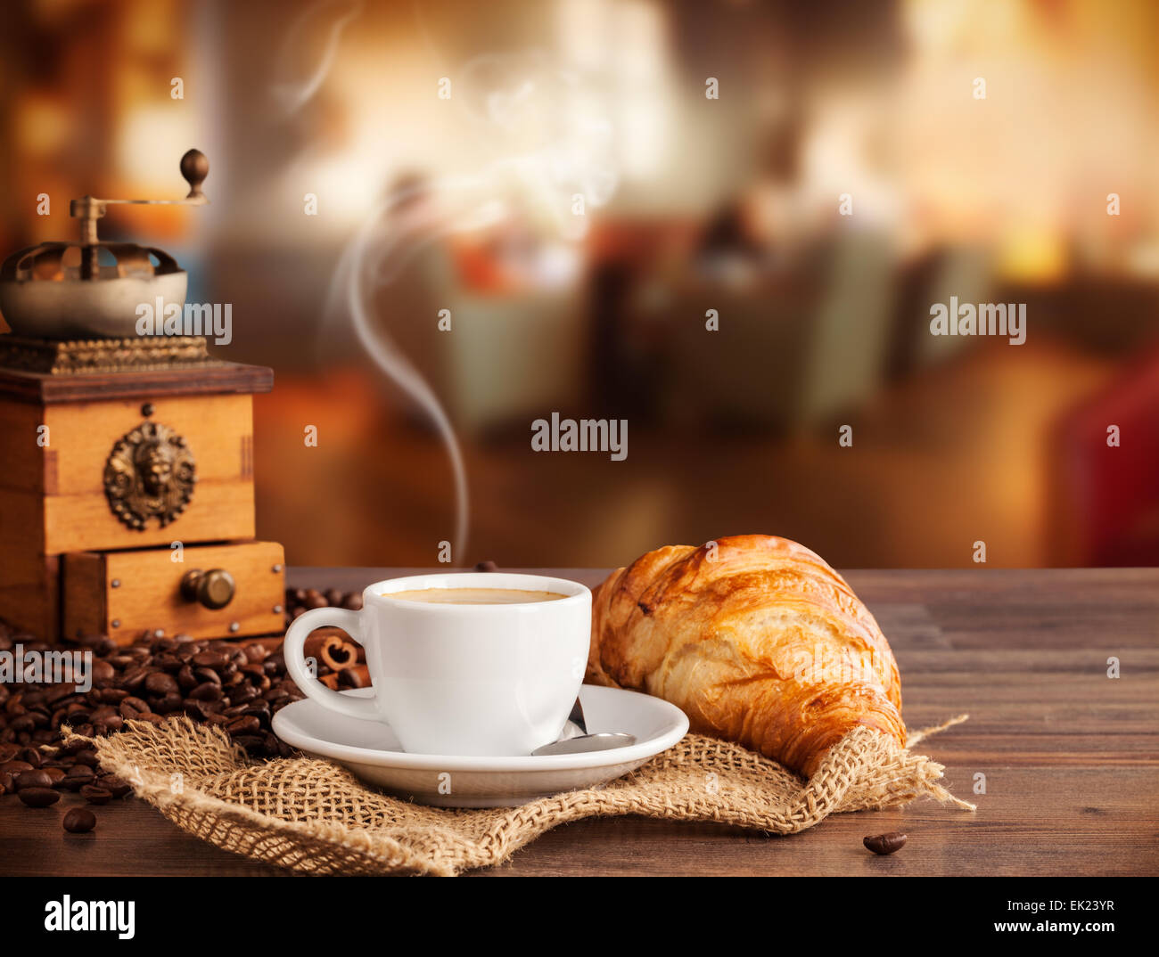 Coffee drink served with croissant on wooden table with blur cafeteria as background Stock Photo