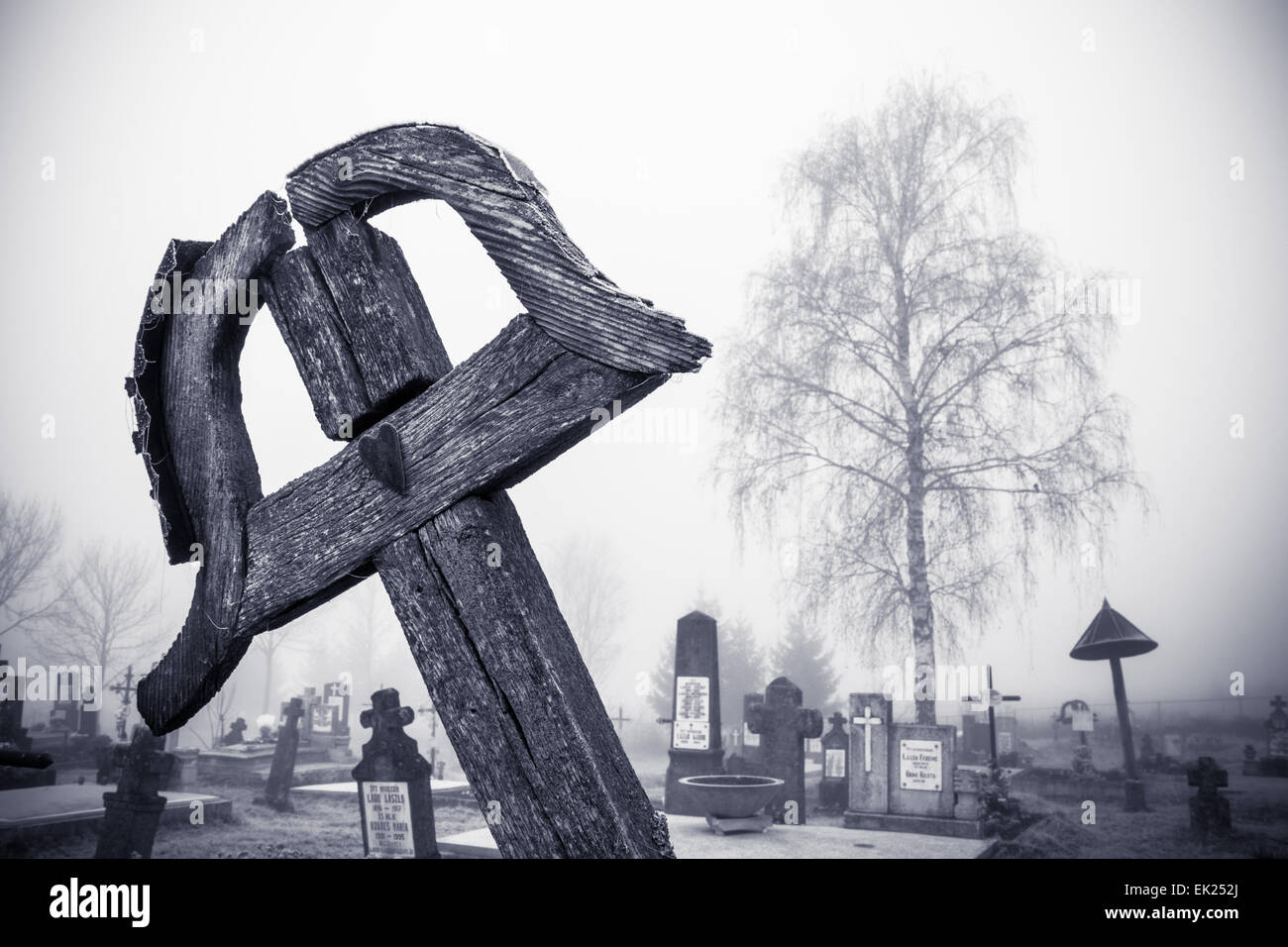 Wood grave-cross with heart on it, cemetery and a tree in the background. Slight vignetting effect to enhance the mood. Stock Photo