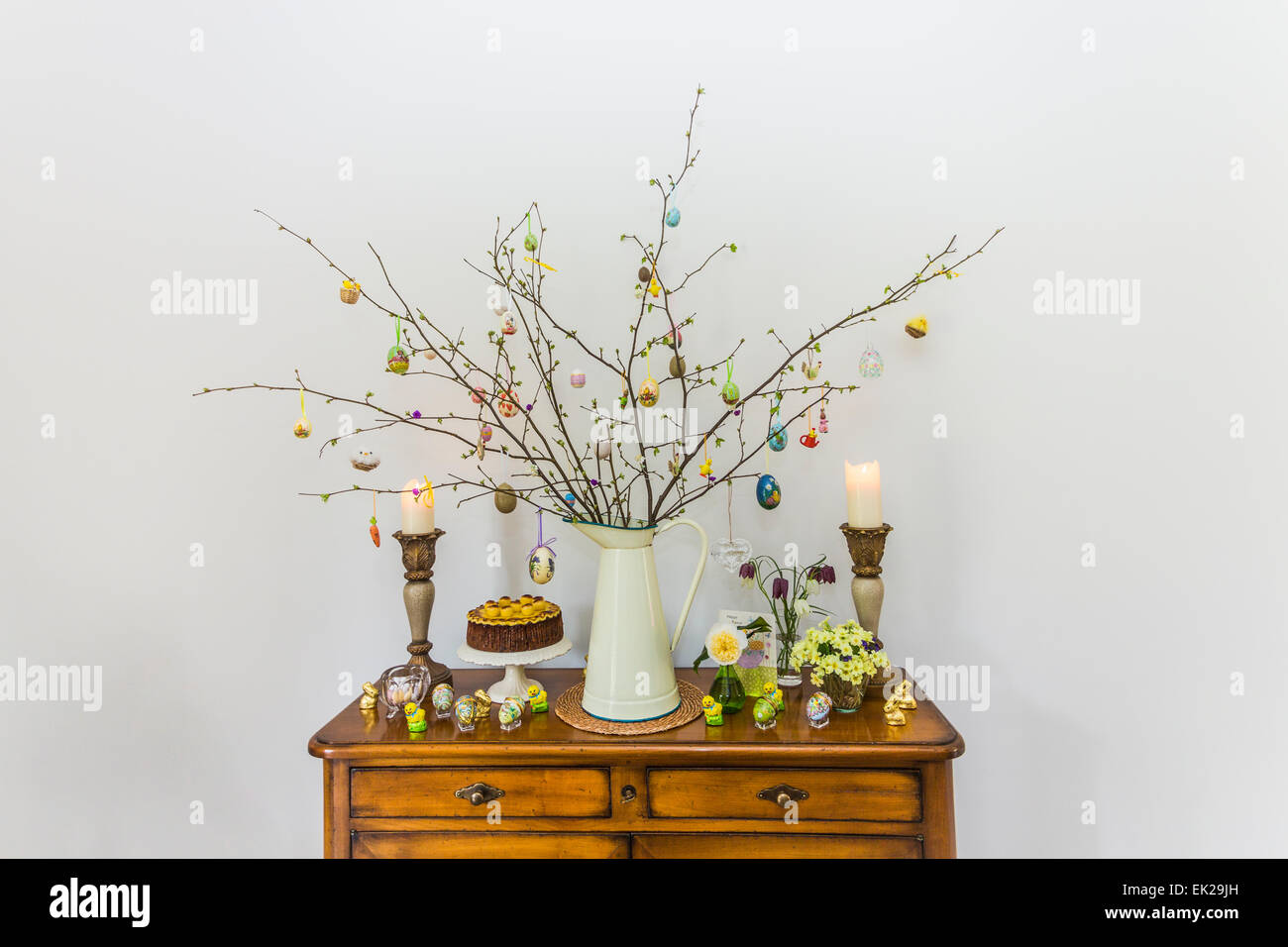 Traditional Easter tree branch arrangement on a sideboard with hanging eggs (Easter egg tree), simnel cake and candles, home made Stock Photo