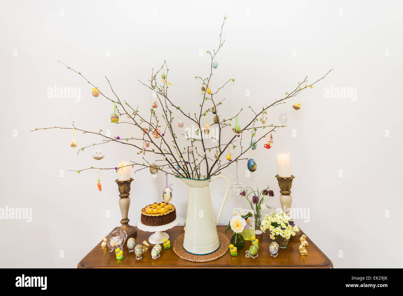 Traditional Easter tree branch arrangement on a sideboard with hanging eggs (Easter egg tree), simnel cake and candles, home made Stock Photo
