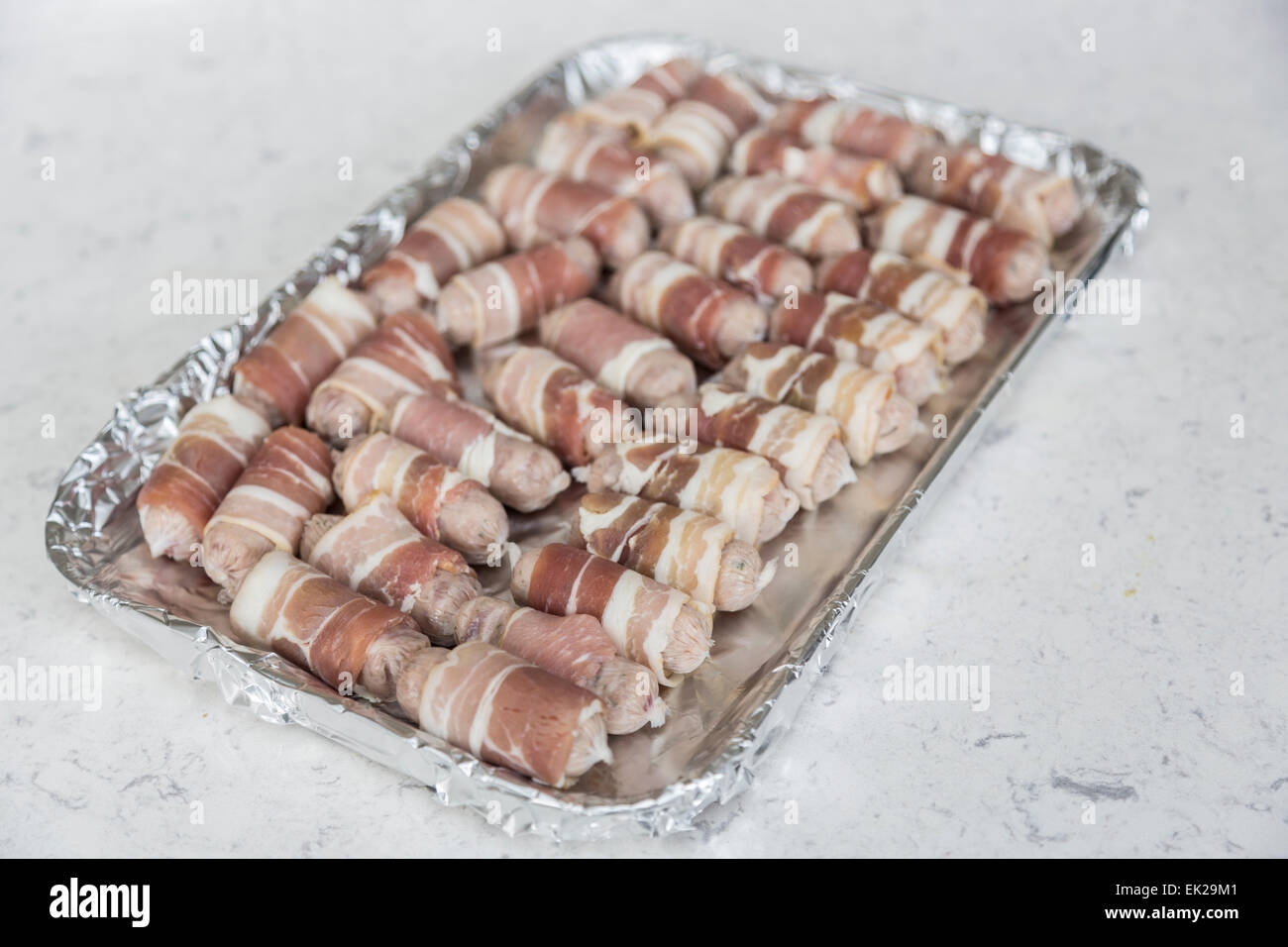 Tray lined in foil with uncooked small sausages wrapped in bacon (pigs