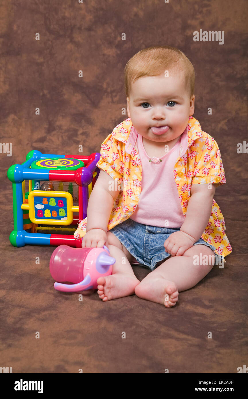 Six month old baby girl with her tongue out, playing with her sippy cup