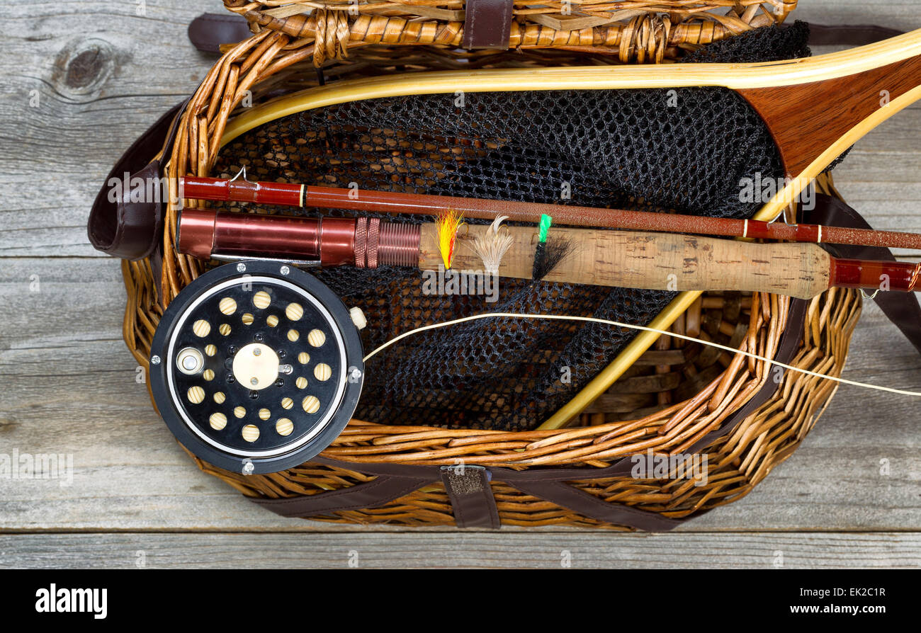 Antique fly fishing reel, rod, flies, and net on top of open creel with rustic wood underneath. Layout in horizontal format. Stock Photo