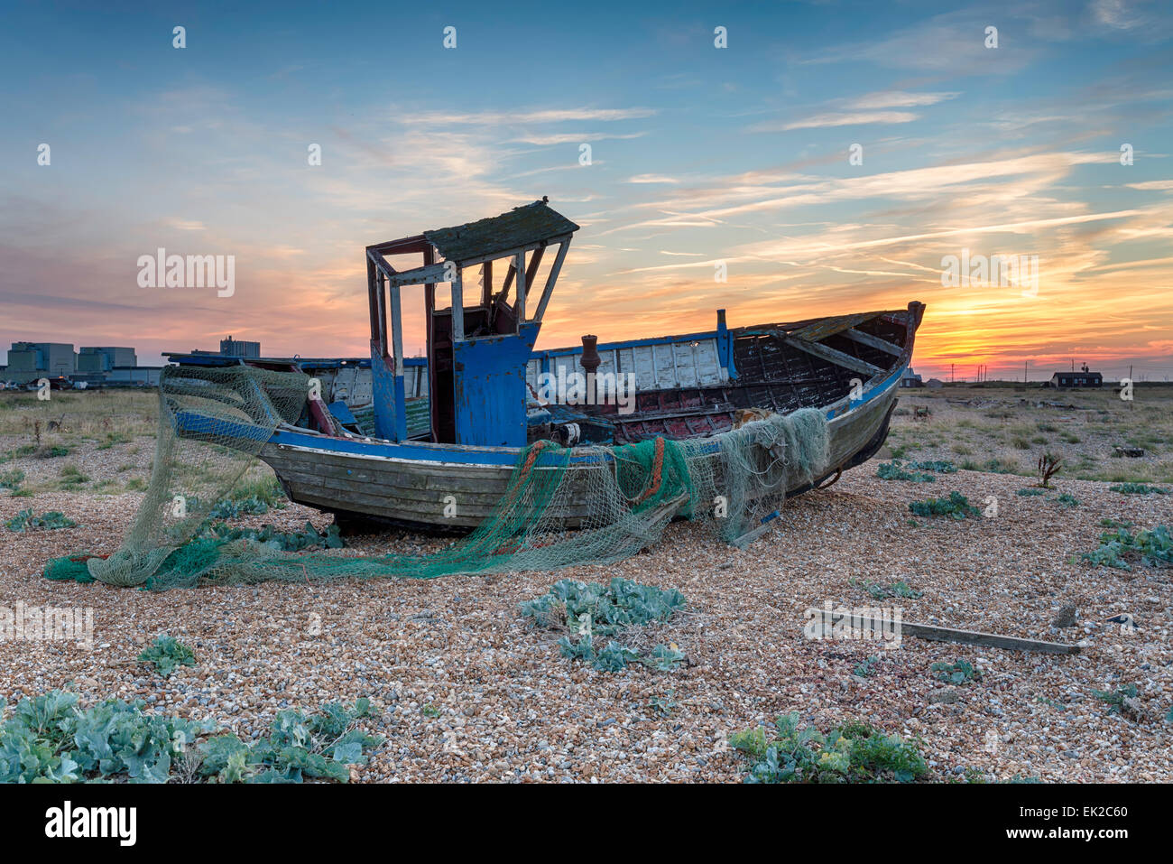 Beautiful dramatic sunset over an old weathered fishing boat with nets on a pebble beach Stock Photo