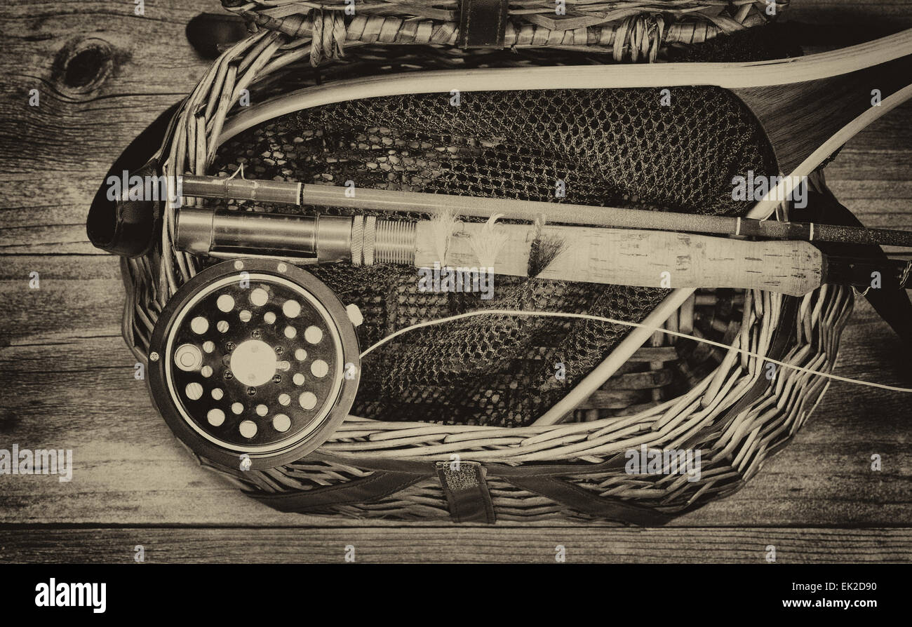Vintage and aging grain concept of an antique fly fishing reel, rod, flies, and net on top of open creel with rustic wood Stock Photo