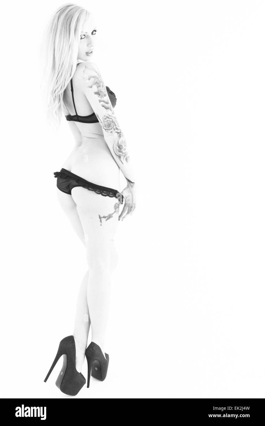 A black and white image of a sexy blond tattooed model in black underwear and high heels. Stock Photo