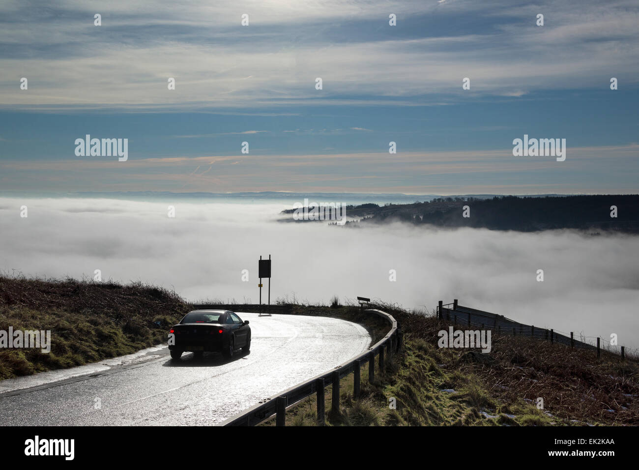 Car travelling downhill above mist covered valley. Stock Photo