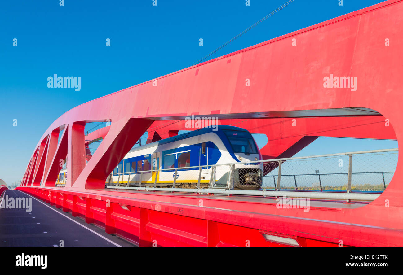 train passing the new red railroad bridge over the IJssel river in the Netherlands Stock Photo