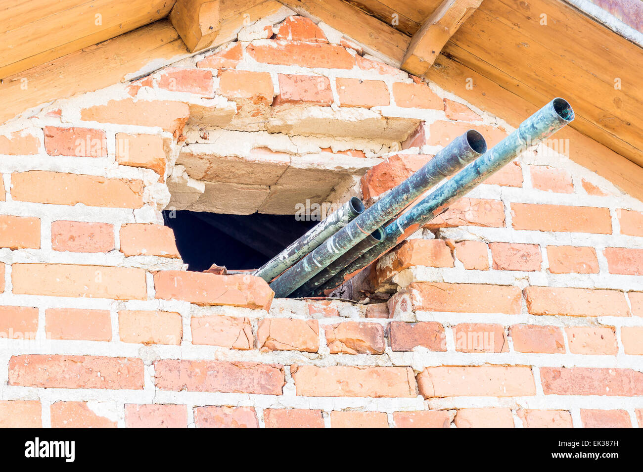 Metal pipes sticking out of a broken brick wall under the roof. Stock Photo