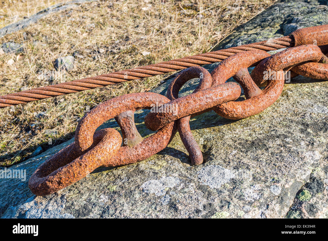 Old rusty chain and wire set in the rock to anchor heavy equipment. Stock Photo