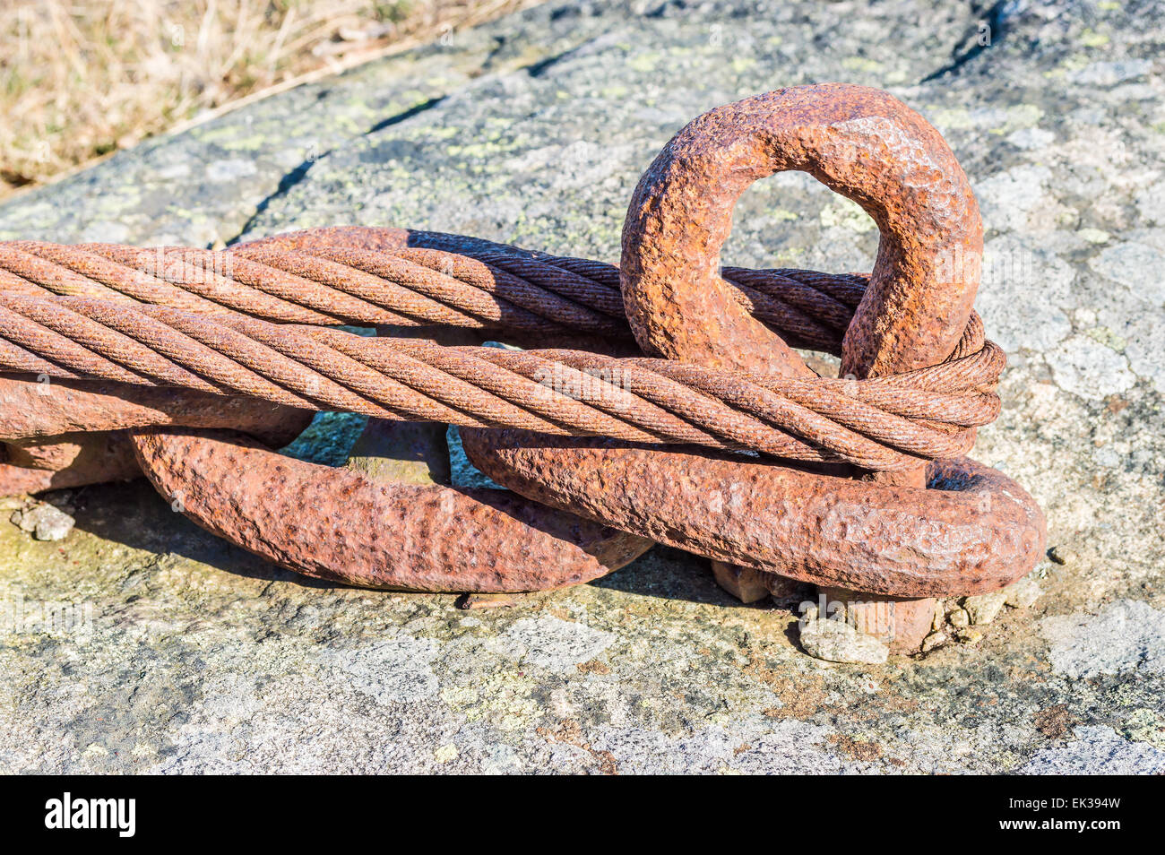 Rusty old chain and wire looped and anchored to the rock face to secure heavy loads. Stock Photo