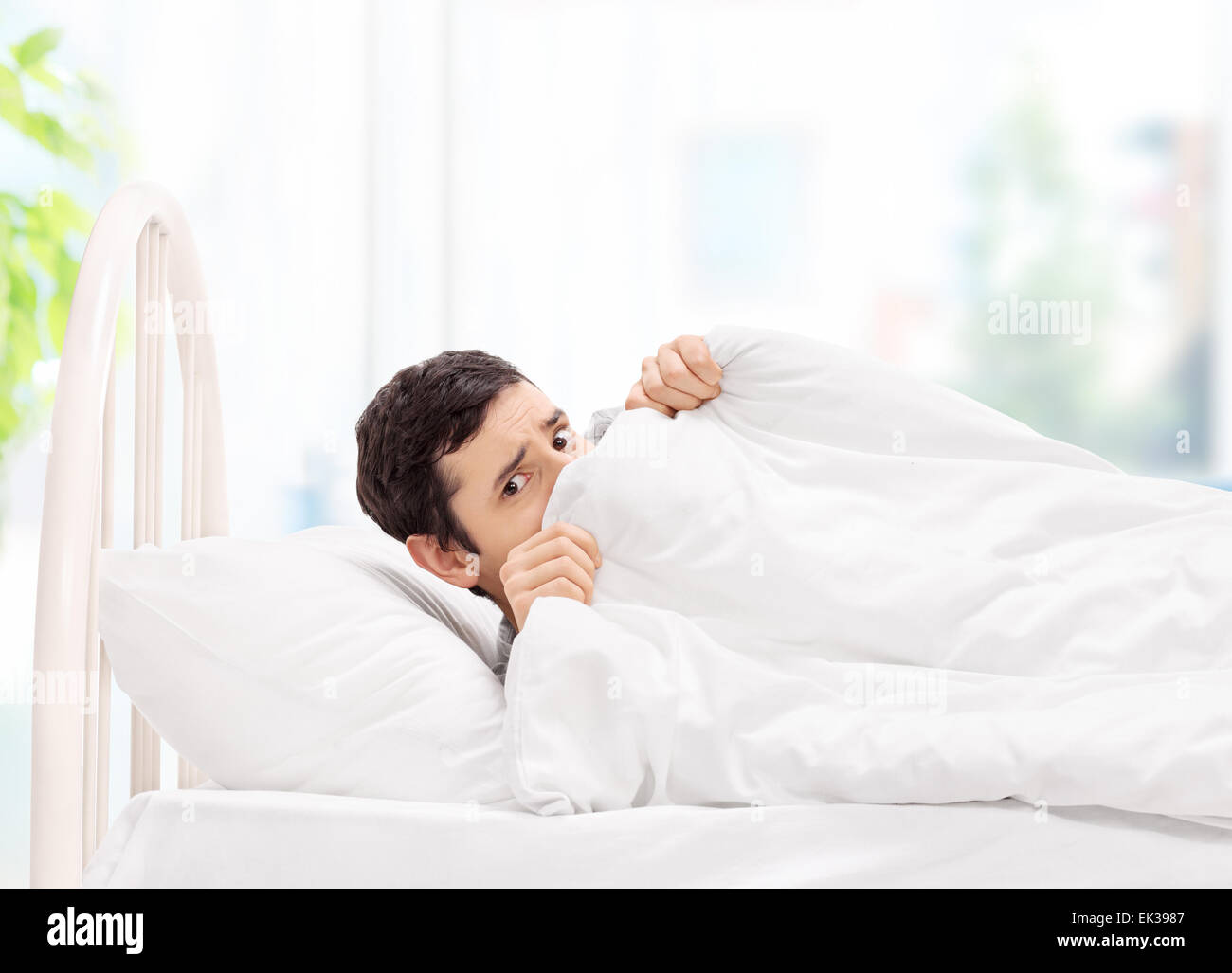 Scared guy lying in bed and hiding under a blanket at home Stock Photo -  Alamy