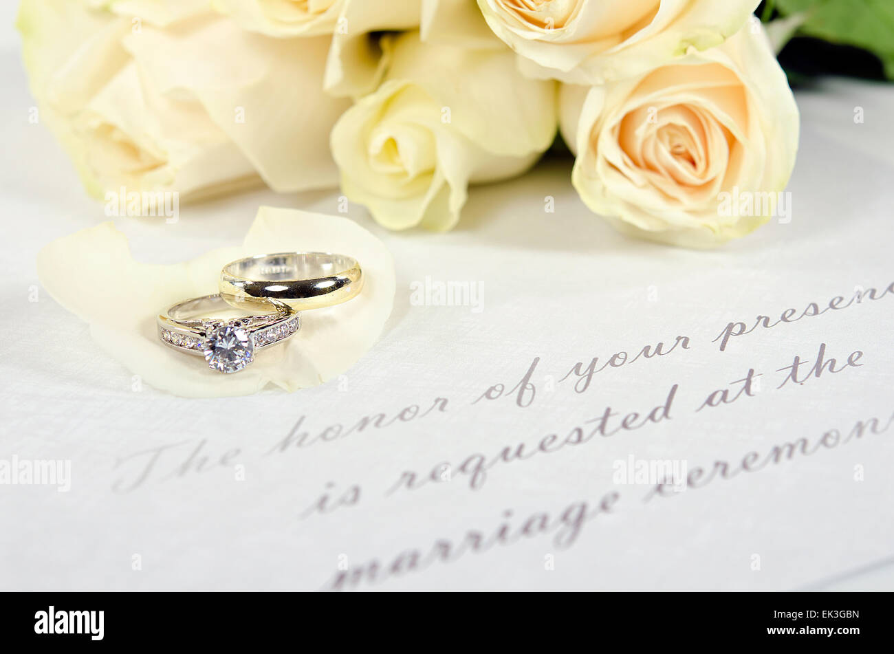 wedding rings on white rose petals with invitation Stock Photo
