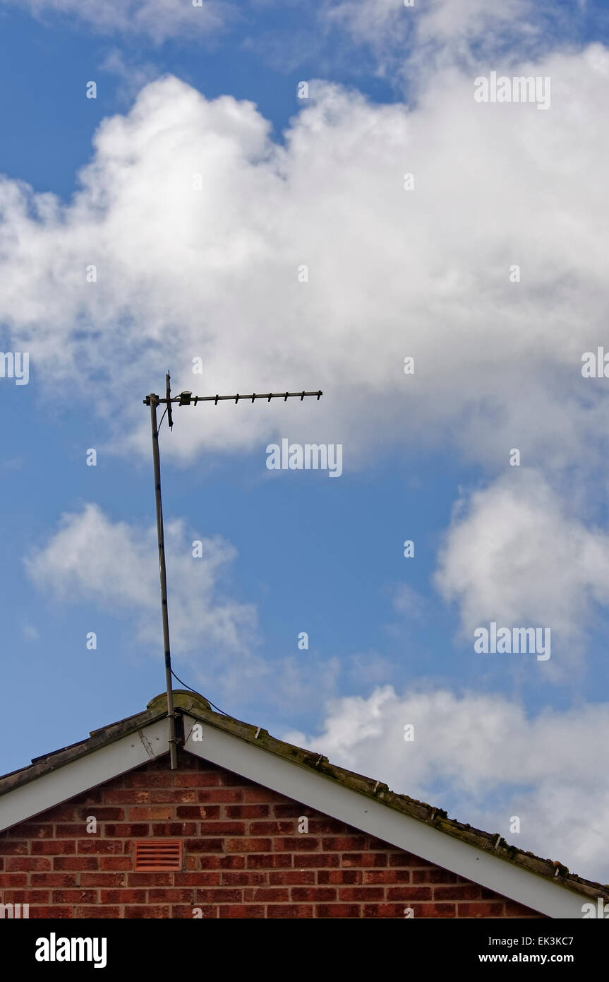 Basic television aerial/antenna on the roof of a house against blue sky with white clouds. Stock Photo