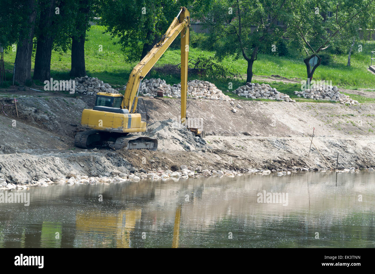 Yellow Excavator at Riverbank Performing River Regulation Works Stock Photo