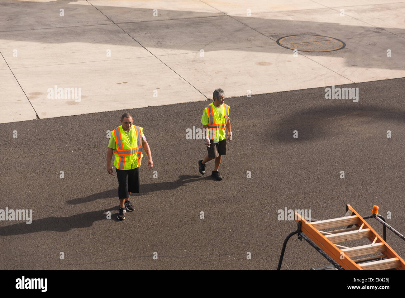 Airport workers walking on a tarmac wearing bright green orange safety vests Stock Photo