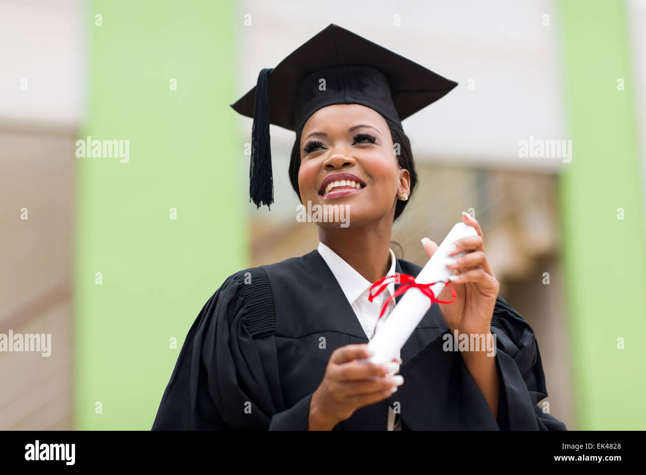 pretty African college student in graduation cap and gown in front of school building Stock Photo