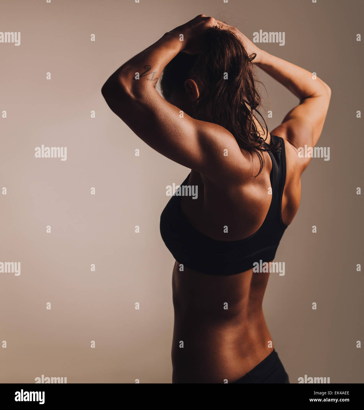Rear view of young woman bodybuilder showing muscular body. Fitness female showing muscular back. Stock Photo
