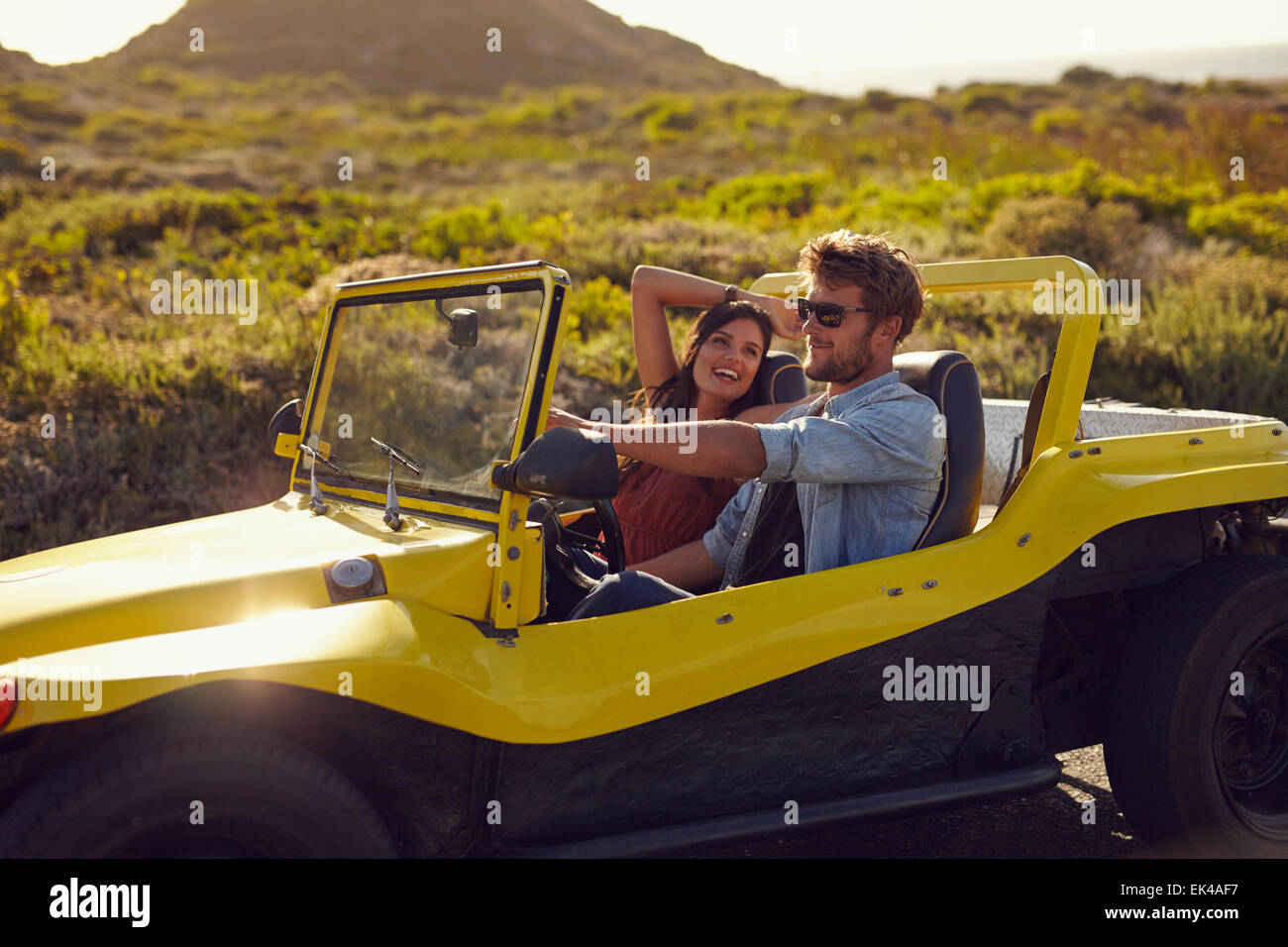 Portrait of happy young couple on a road trip in a beach buggy. Smiling young woman with her boyfriend driving car in countrysid Stock Photo