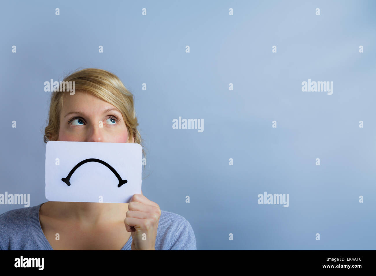 Unhappy Portrait of a Woman Holding a Sad Mood Board with Blue Background Stock Photo
