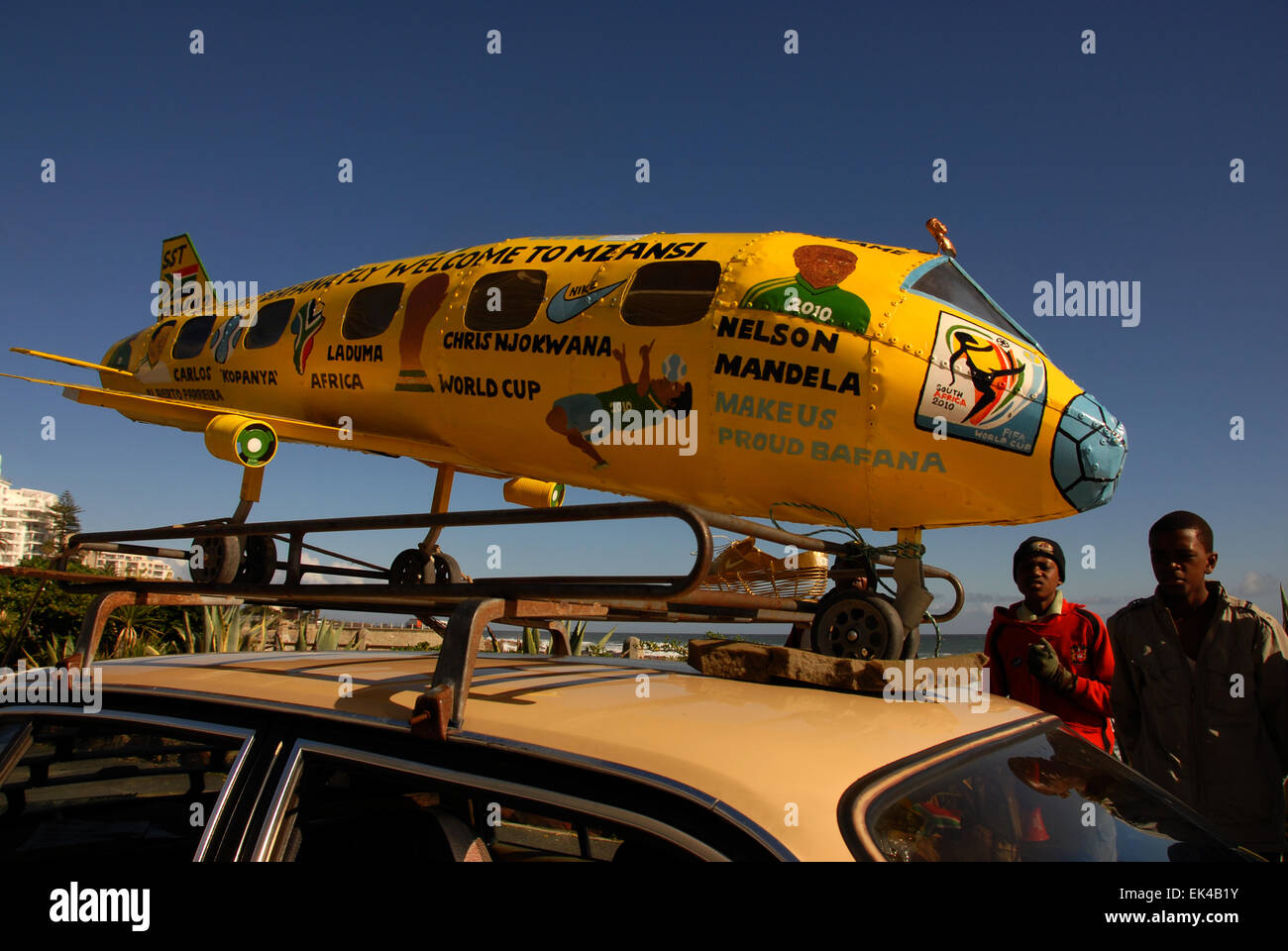 Two young men stand next to their car with a home made areoplane on the car to celebrebrate the 2010 FIFA World Cup in South Africa, Sea Point, Cape Town 09.06.2010. The aeroplane is made by Mboneli Lefty Booi and Siseko Christopher Kameso, both from Khayelitsha, a township in Cape Town.The plane is handmade and designed by them. It has been hand painted with a picture of Mandela, zakumi ( the south African world cup mascot), Zuma, Bafana Bafana etc It has all the flags painted on it of the countries taking part. They also made the boot. Their wish was,  “ we would like support from government Stock Photo