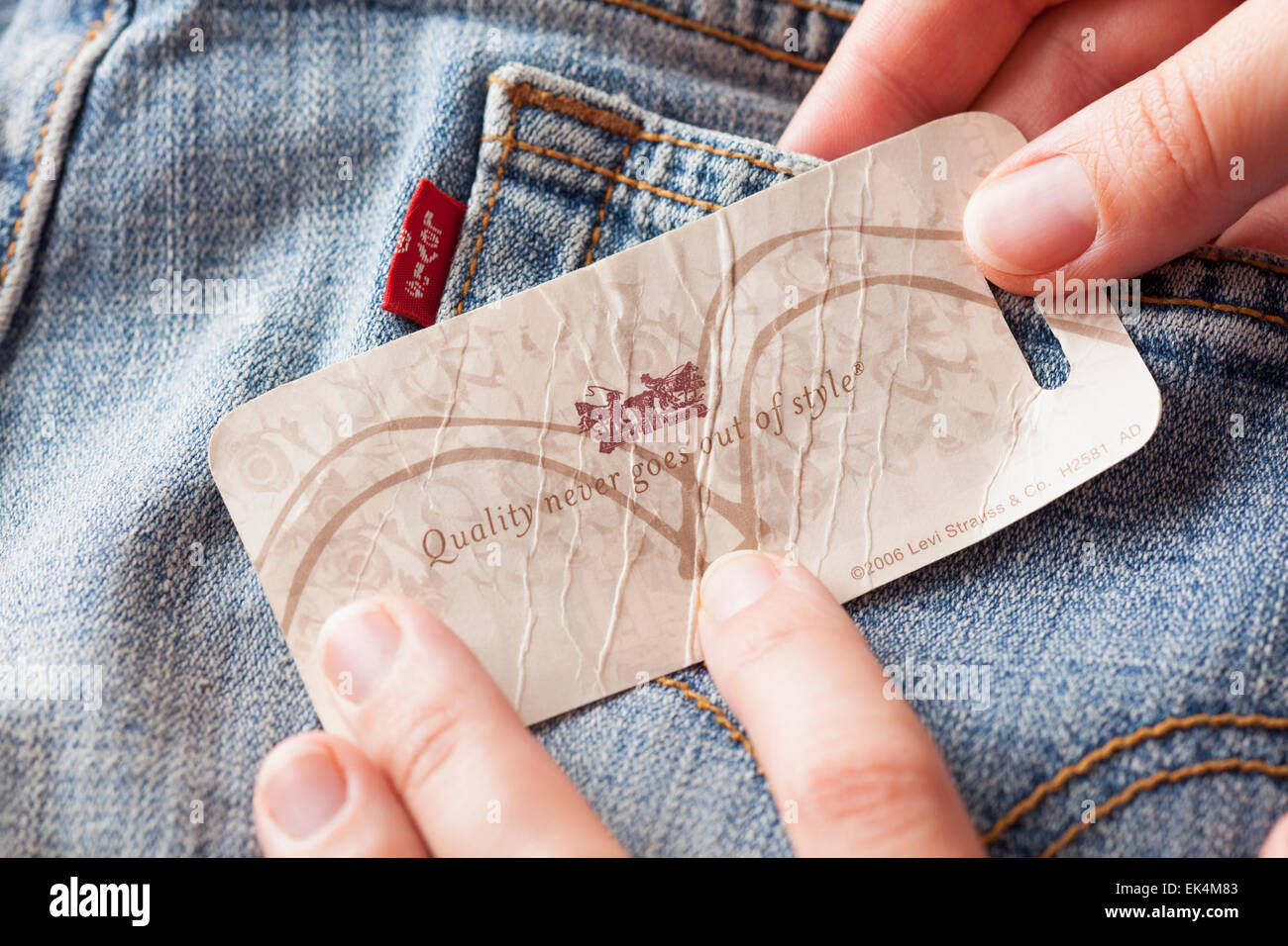 Woman's hand taking label logo with phrase «Quality never goes out of style» on the pair Levi's Jeans. Stock Photo
