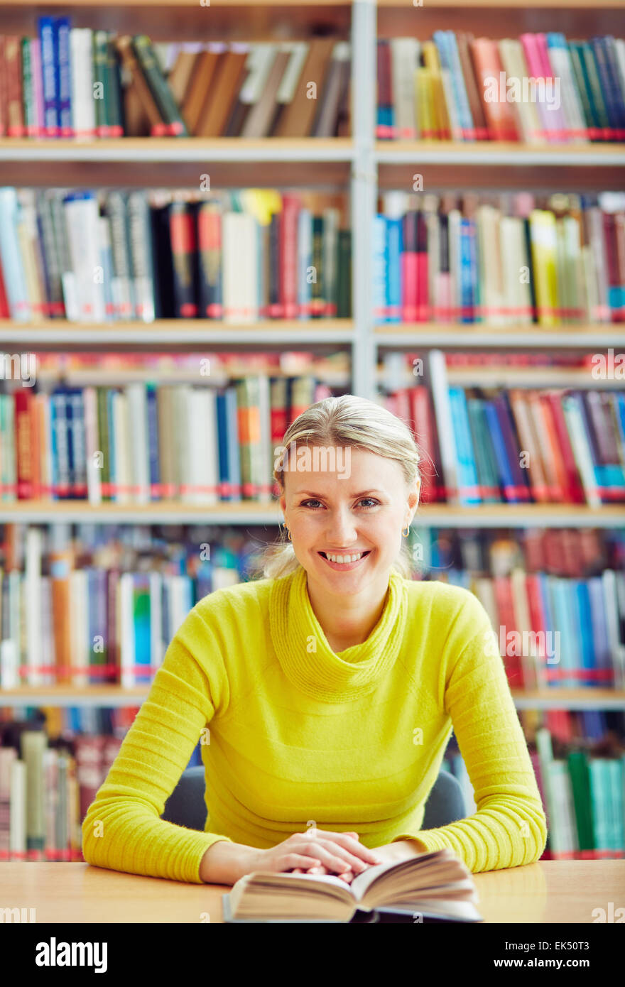 Teenage girl sitting in library with interesting book Stock Photo - Alamy
