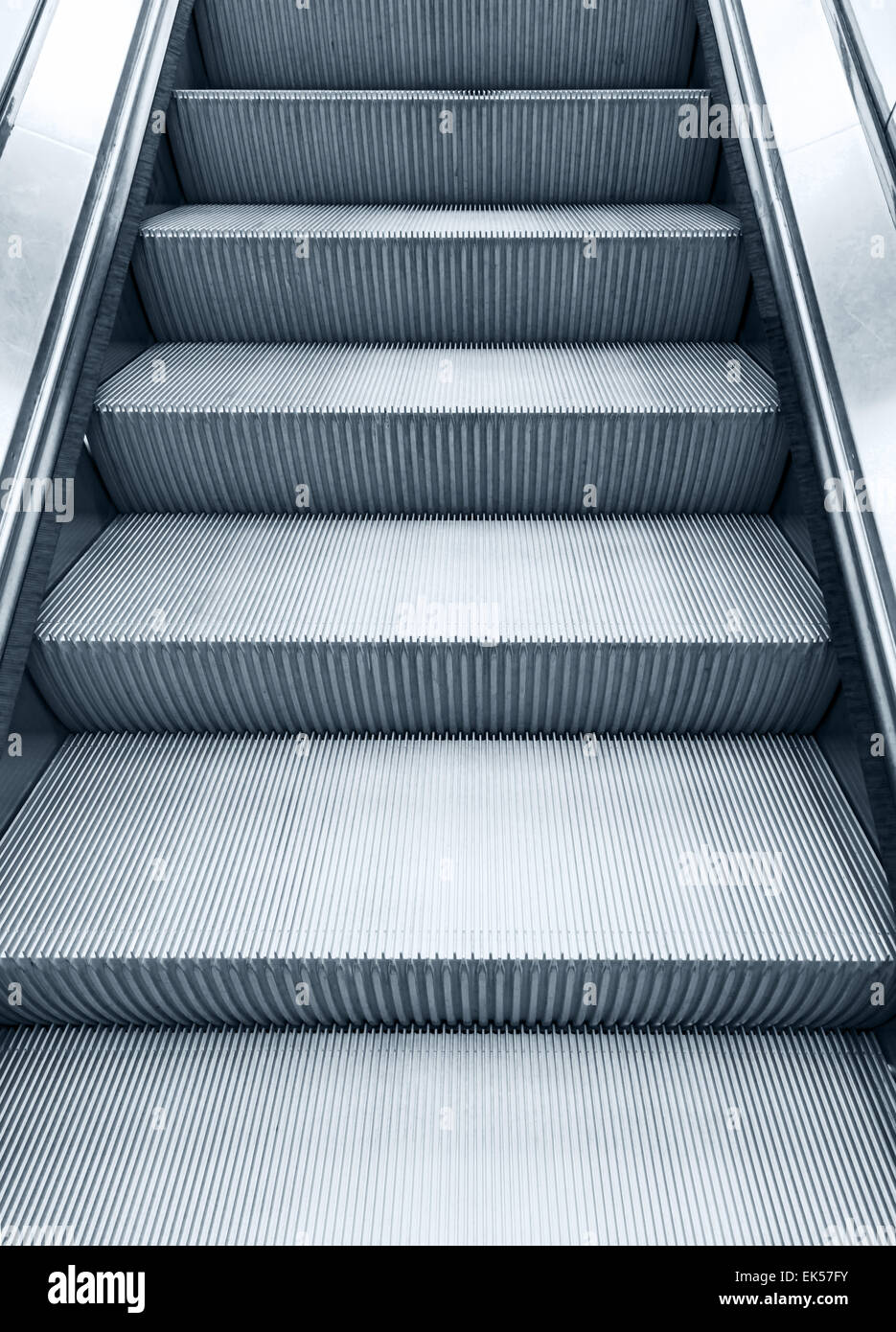 Shining metal escalator moving up, vertical monochrome photo with blue toning filter effect Stock Photo