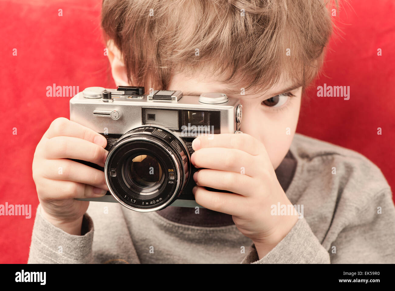 Little girl holding retro camera and looking through the viewfinder. Childhood lifestyle moment of creativity and exploration. Stock Photo