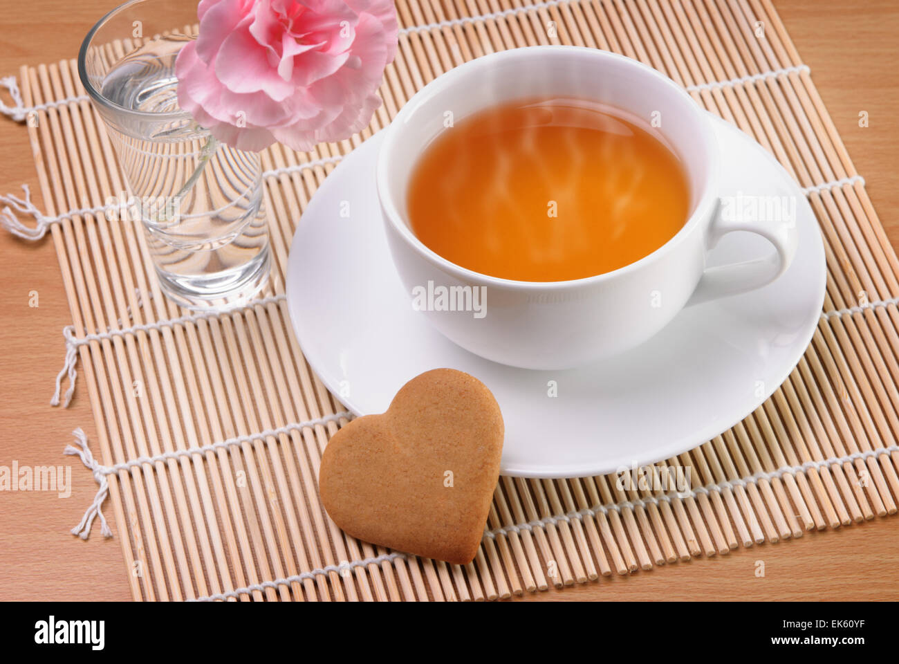 White cup of tea with a heart shaped biscuit and a flower Stock Photo
