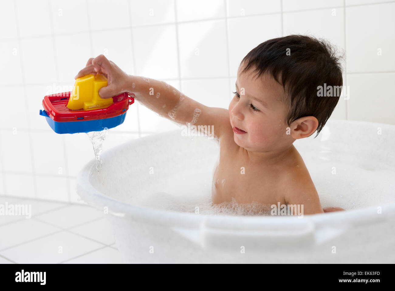 Two year old boy playing in the bath tub with a plastic boat Stock Photo