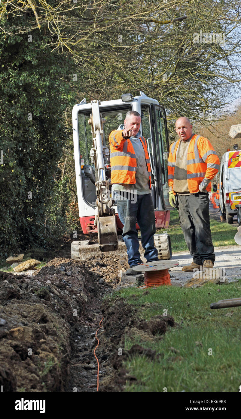 workmen use a mini excavator to install new high speed broadband fibre optic cables in a rural Oxfordshire village Stock Photo
