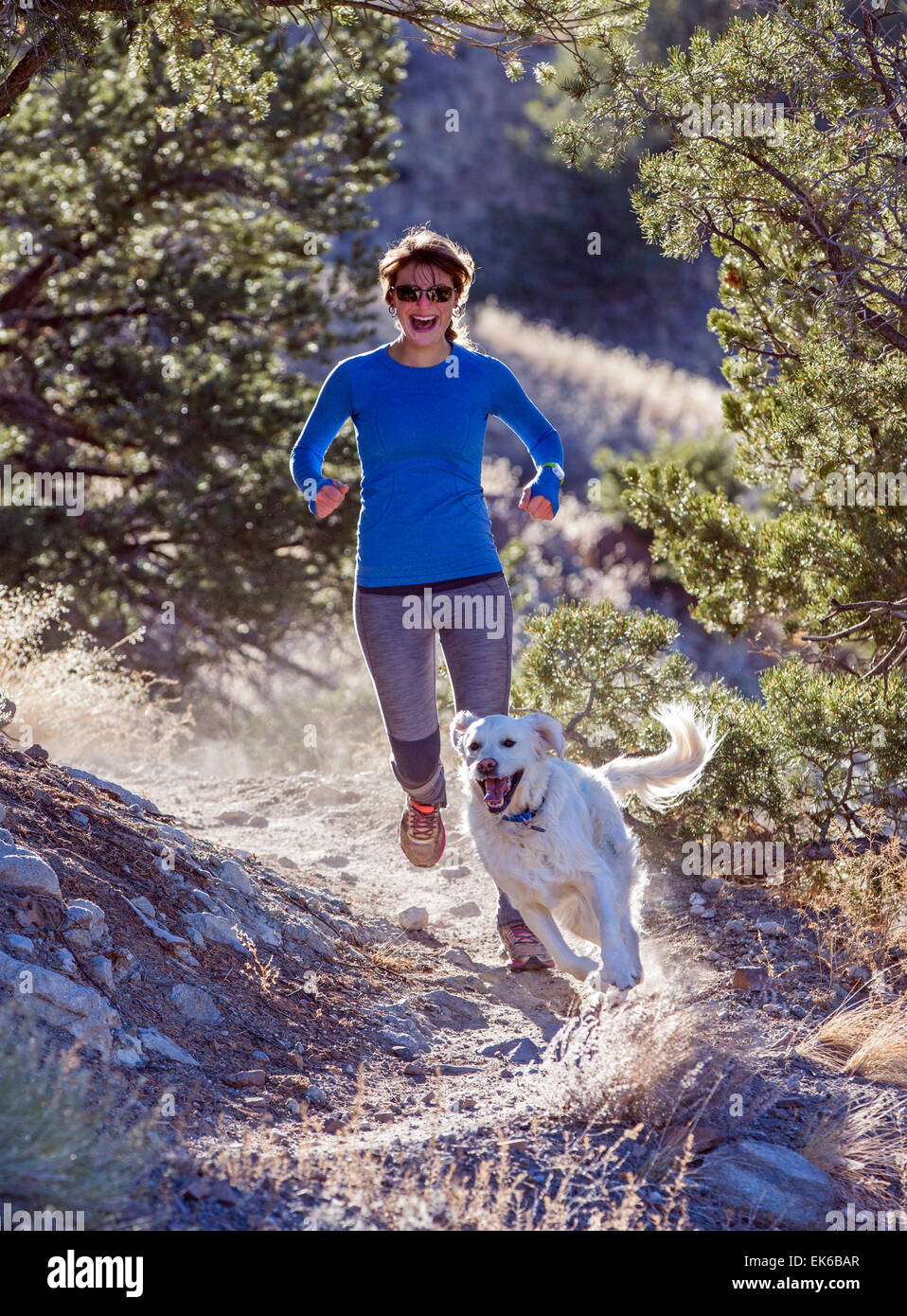 Happy beautiful young woman & dog running on mountain trails near Salida, Colorado, USA Stock Photo