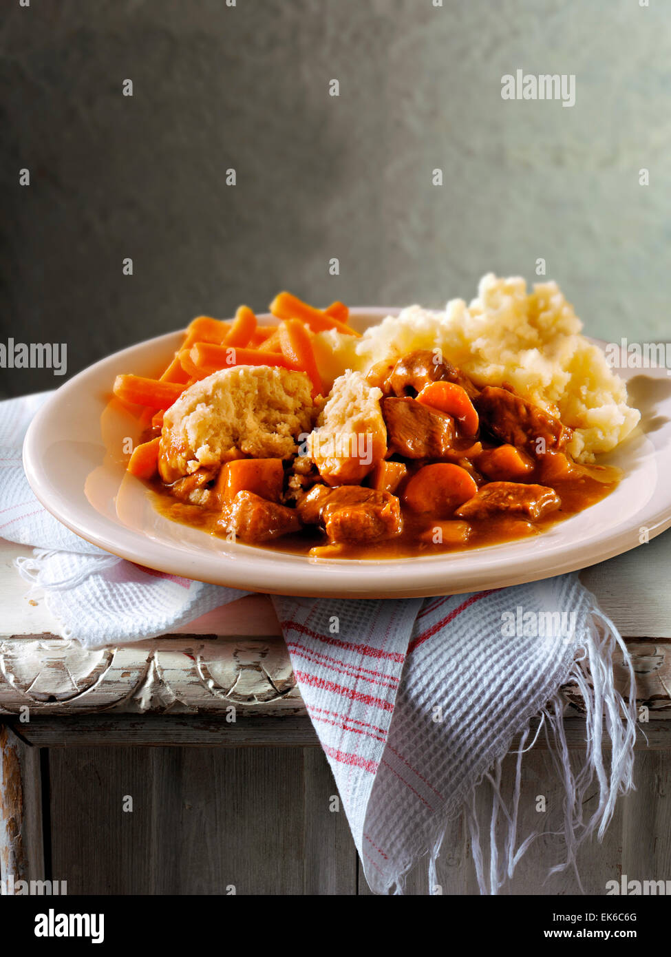 Traditional British cooked Beef Stew nd Dumplins on a white plate in a traditional kitchen setting ready to eat Stock Photo