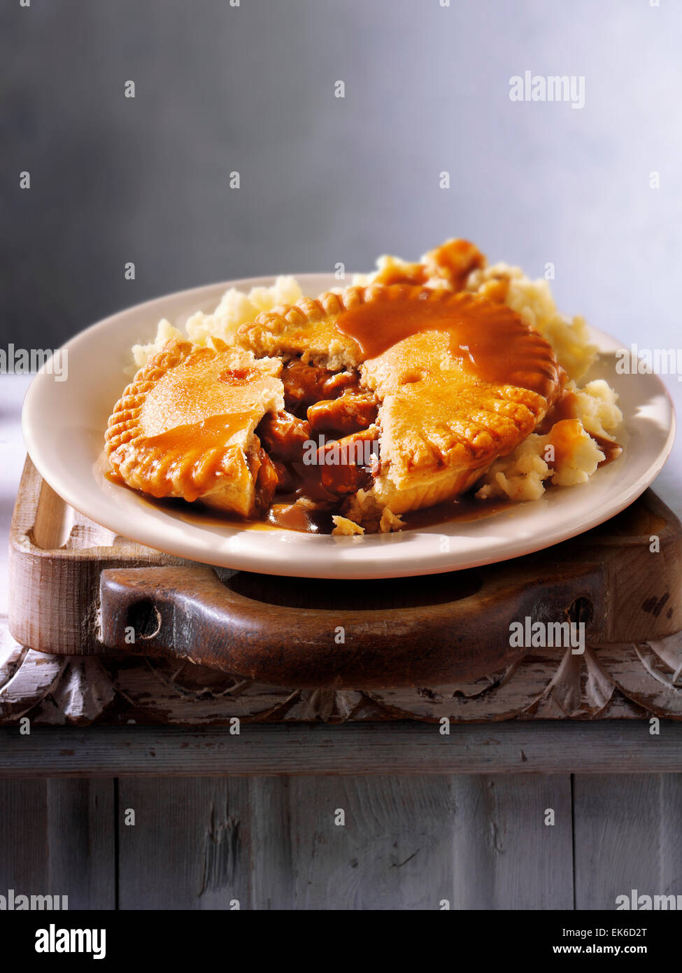 Cooked meal of traditional British beef steak in ale pastry pie & mashed potato served on a plate in a rustic table setting Stock Photo