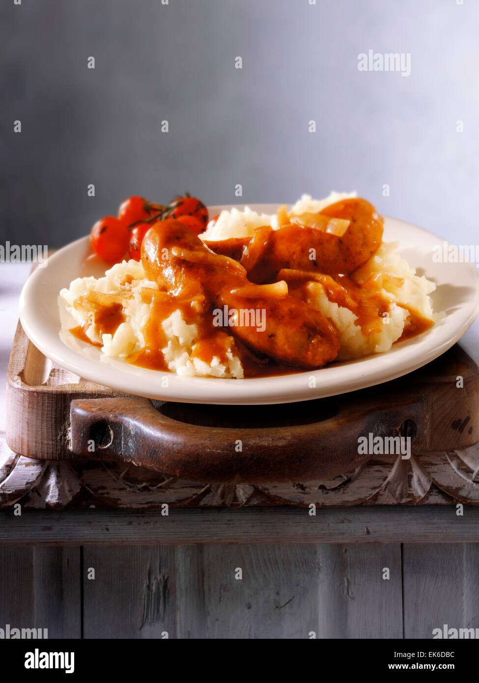 Cooked meal of Cumberland sausages, onion gravy & mashed potatoes served on a plate in a rustic table setting Stock Photo