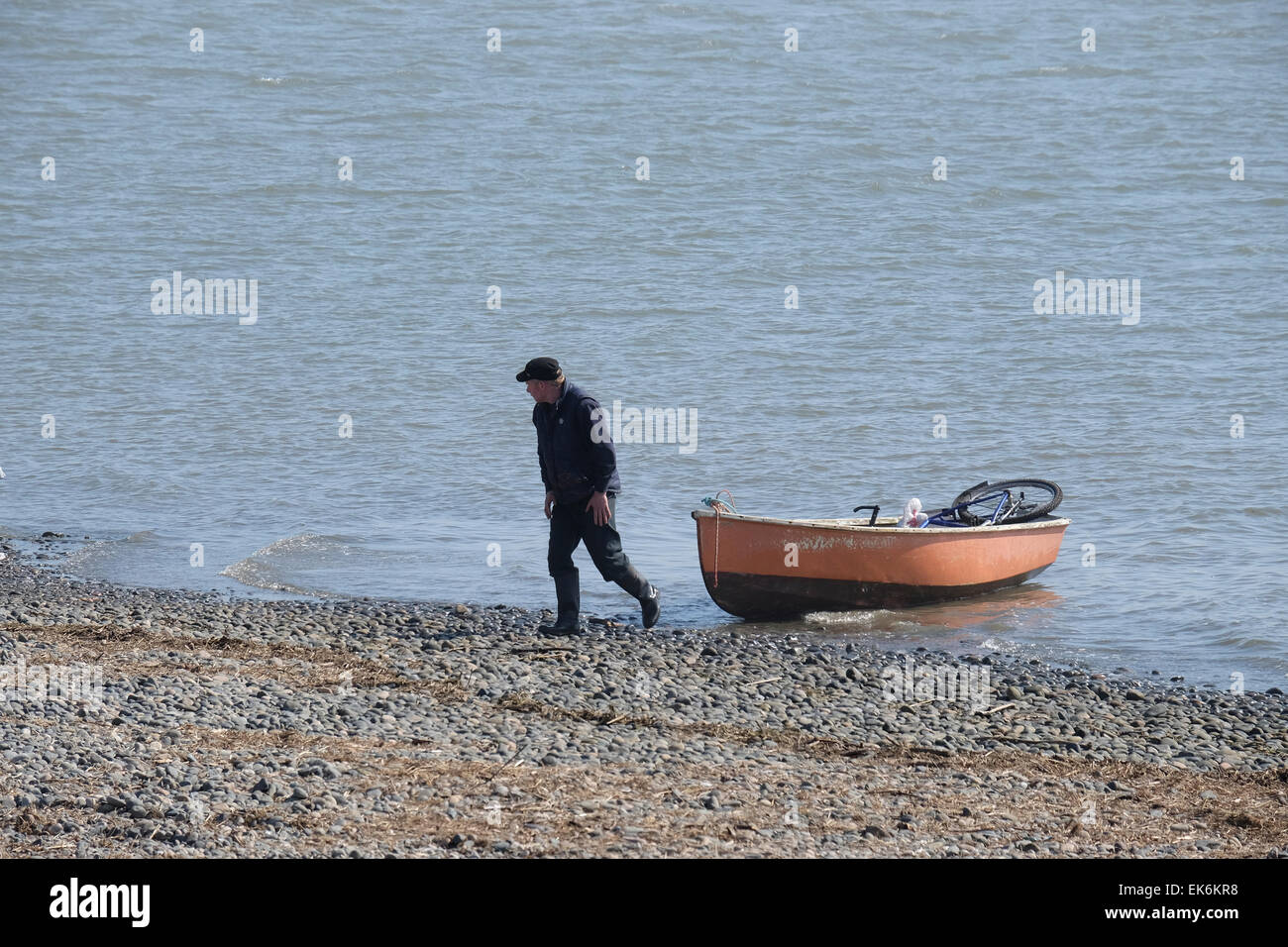 Man leaves Rowing Boat containing bicycle on the shore at Lytham St Annes Stock Photo