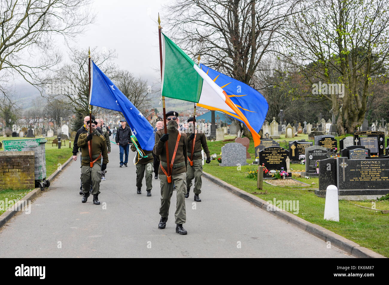 Men dressed in Irish paramilitary uniforms, with their faces covered by military scrim scarves carry Irish flags in Milltown cemetery, during the annu Stock Photo