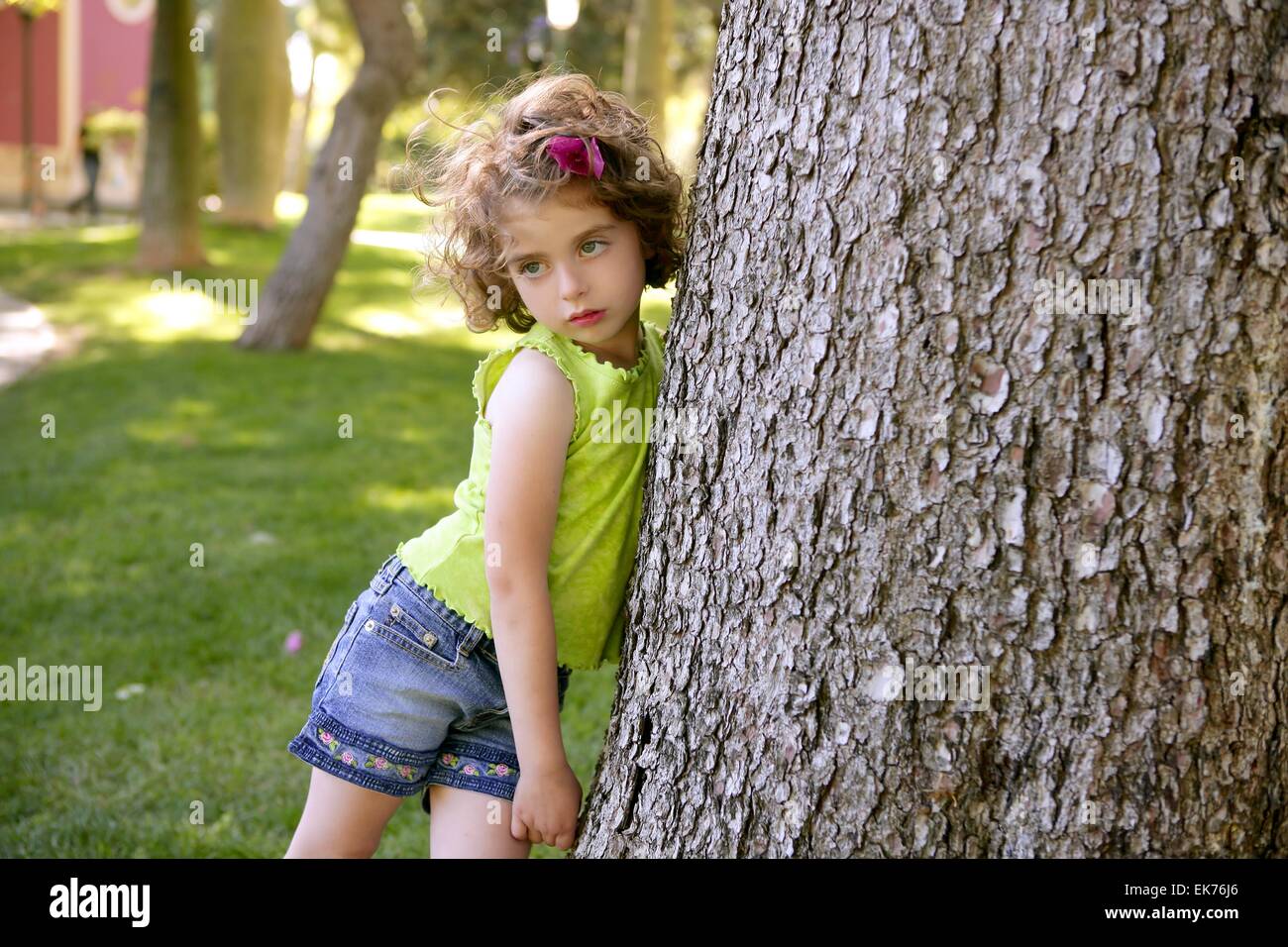 Beautiful little brunette girl beside a tree trunk Stock Photo.