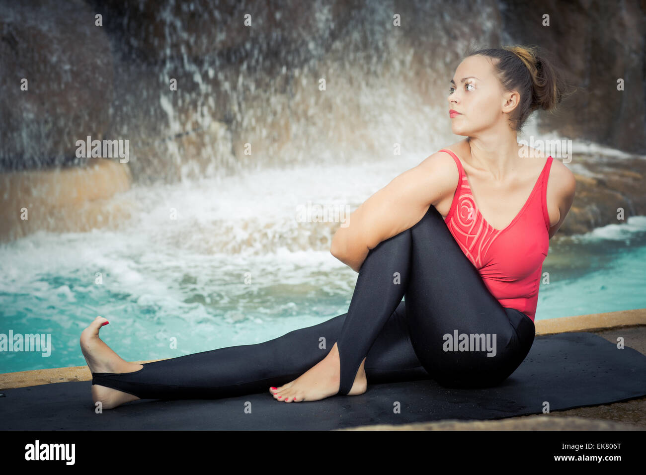 Woman practicing yoga near waterfall. Sage Twist. Marichyasana Stock Photo