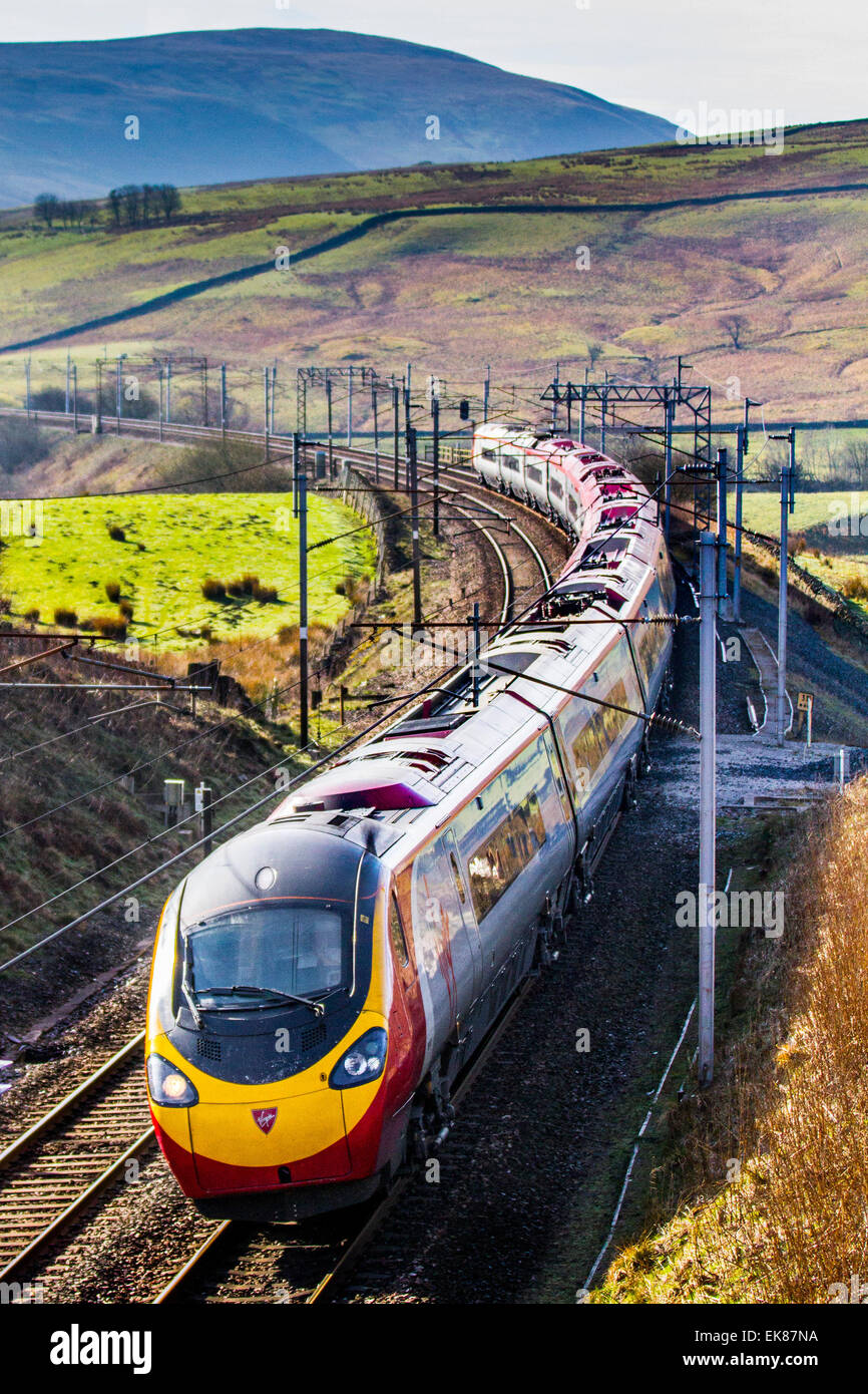 Power lines, and gantries, electric trains at Cumbria, UK 8th April, 2015.  UK Weather.  Bright Sunny day over the Cambrian Fells and West Coast Settle to Carlisle Line Rail Traffic.  Class 390 Pendolino is a type of electric high-speed train operated by Virgin Trains in the United Kingdom. They are electric multiple units using Fiat Ferroviaria's tilting train Pendolino technology and built by Alstom. Fifty-three 9-car units were originally built between 2001 and 2004 for operation on the West Coast Main Line (WCML), with an additional four trains and 62 cars built between 2009 and 2012. Stock Photo