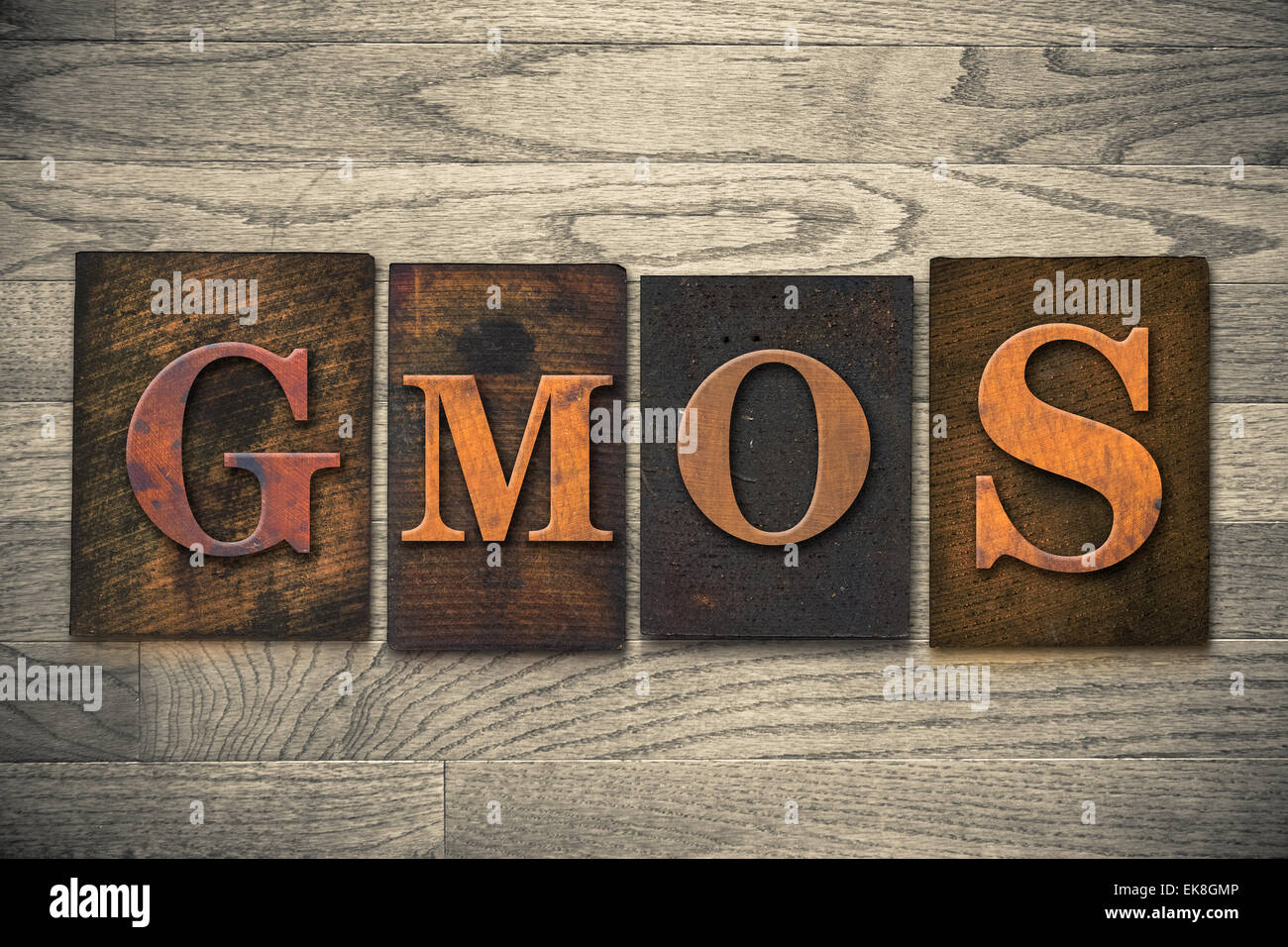 The word "GMOs" theme written in vintage, ink stained, wooden letterpress type on a wood grained background. Stock Photo