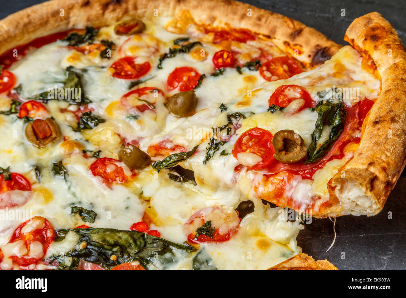 A close up view of home made thin crust pizza slice with olives tomatoes peppers basil mozzarella cheese, London UK Stock Photo