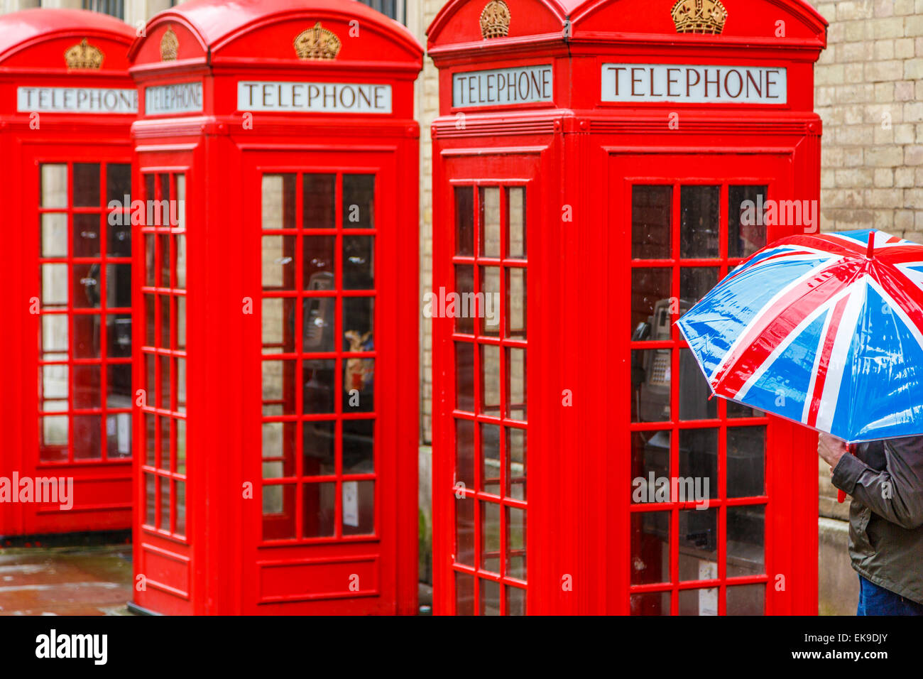 Red London Telephone boxes in the rain with a person holding a Union Jack Umbrella walking past, London England UK Stock Photo
