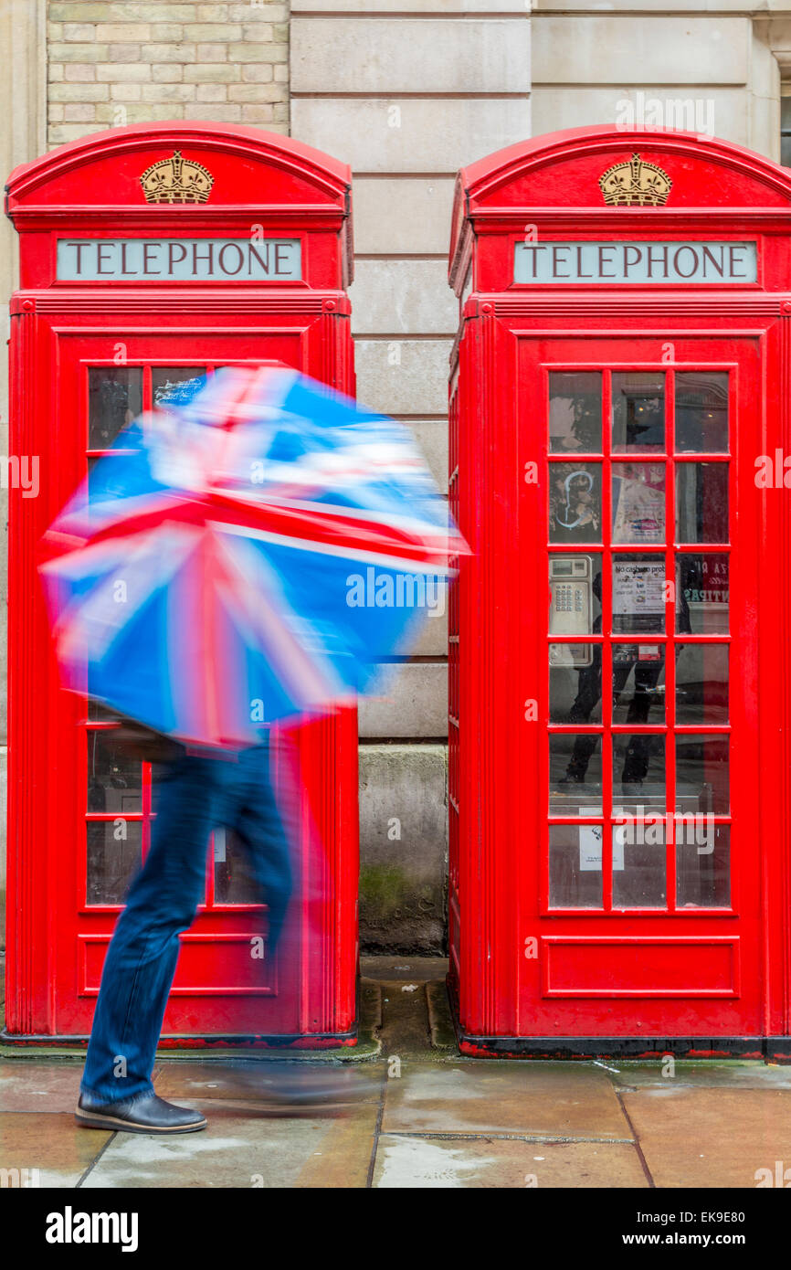 Red London Telephone boxes in the rain with a person holding a Union Jack Umbrella London England UK Stock Photo